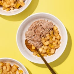 white bowls with buckwheat porridge, diced cooked pears and a gold spoon on yellow background