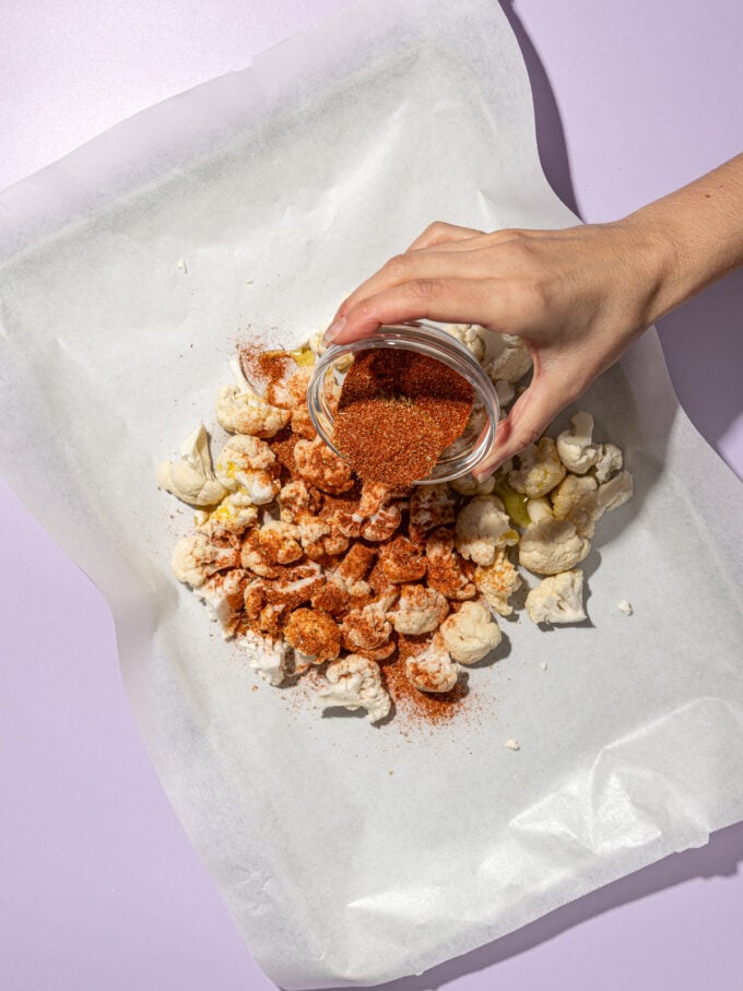 hand shaking spices on cauliflower on baking sheet