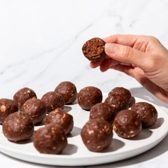 hand holding chocolate protein ball above plate of balls