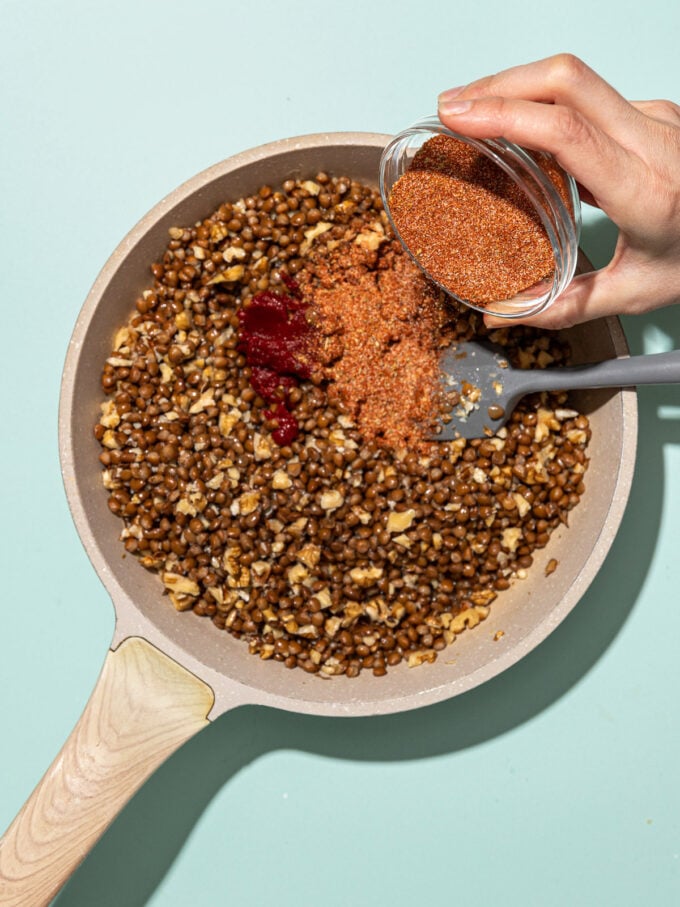 hand pouring taco seasoning into skillet with lentils and walnuts