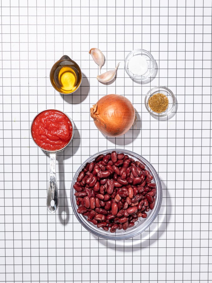 glass bowl of kidney beans, metal cup of tomato sauce, onion, garlic, oil, salt and cumin