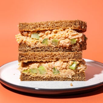stacked chickpea salad sandwich on white plate with orange background