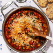 skillet with cheesy white beans in pizza sauce and wooden spoon beside sliced bread and fresh basil