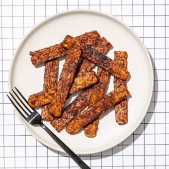slices of tempeh bacon on white plate with black fork