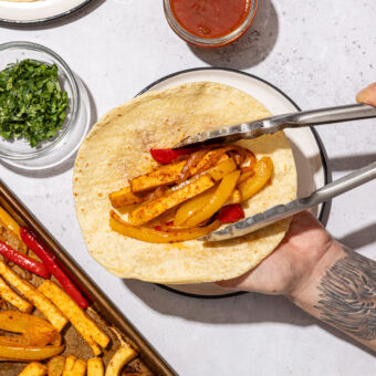 hand with placing tofu onto tortilla with tongs beside salsa and cilantro