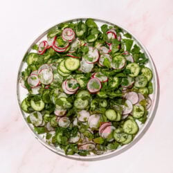 cucumber radish and herb salad on white plate on pink background