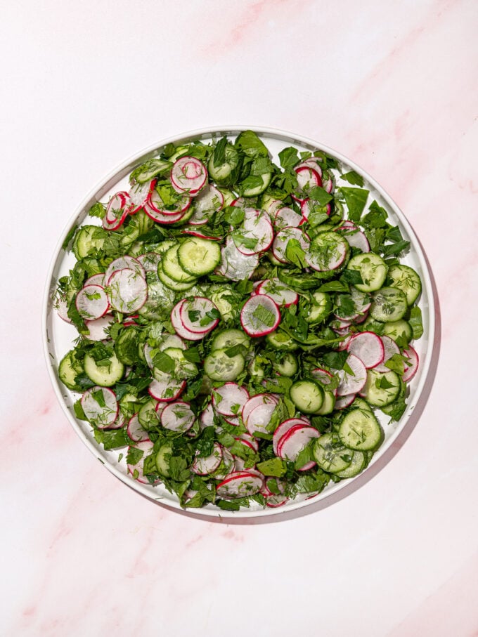 cucumber radish and herb salad on white plate on pink background