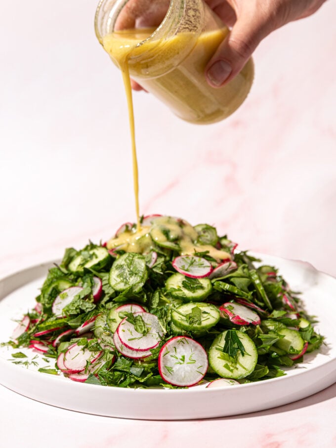 hand pouring lemon dressing on cucumber radish salad on white plate