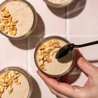 black spoon dipping into glass jars of blended chia pudding with crushed peanuts
