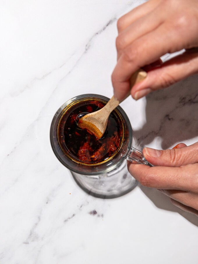 stirring soy and chili sauce with a wooden spoon in glass jar