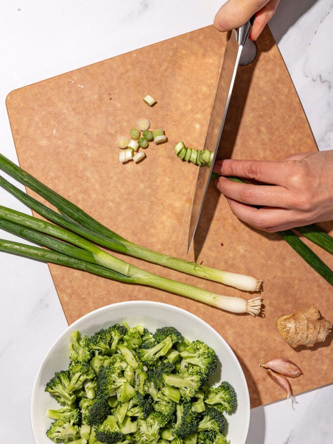 hand slicing green onion on cutting board with knife