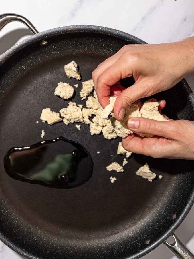 hand crumbling tofu into nonstick skillet