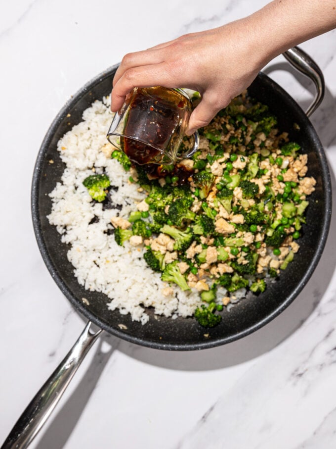 hand pouring sauce into skillet with rice, tofu and broccoli