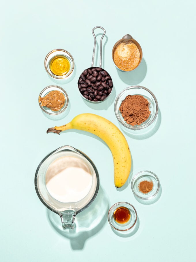 cup of milk with banana, bowls of beans, cocoa, almond butter and espresso