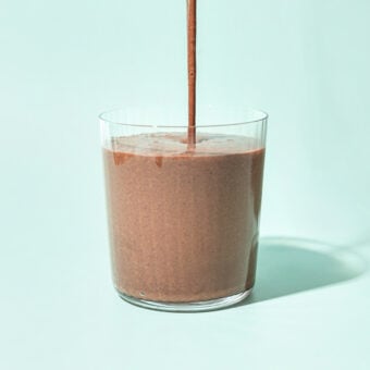 pouring black bean chocolate smoothie into a glass on a blue background
