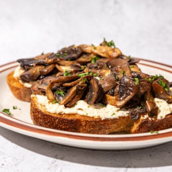 sautéed mushrooms on slices of sourdough toast with tofu ricotta on brown plate