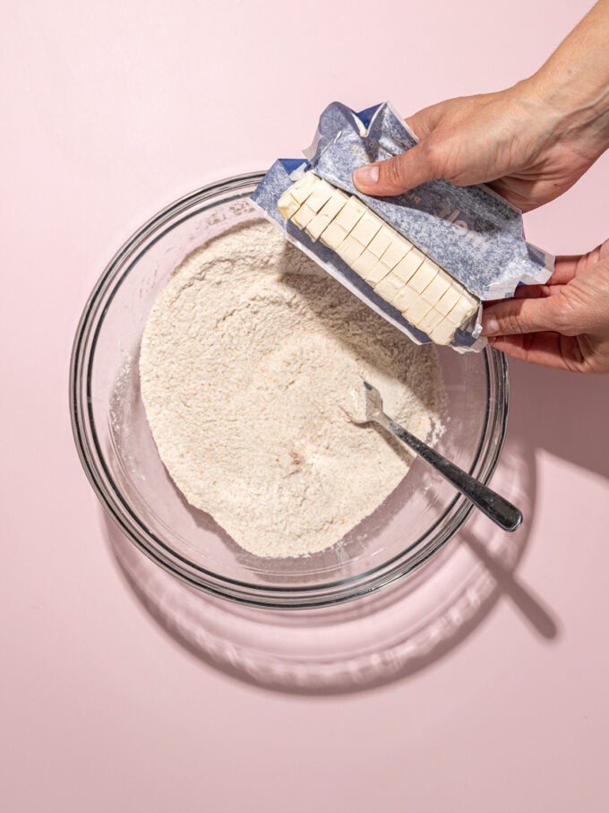 hand adding stick of butter to glass bowl of flour