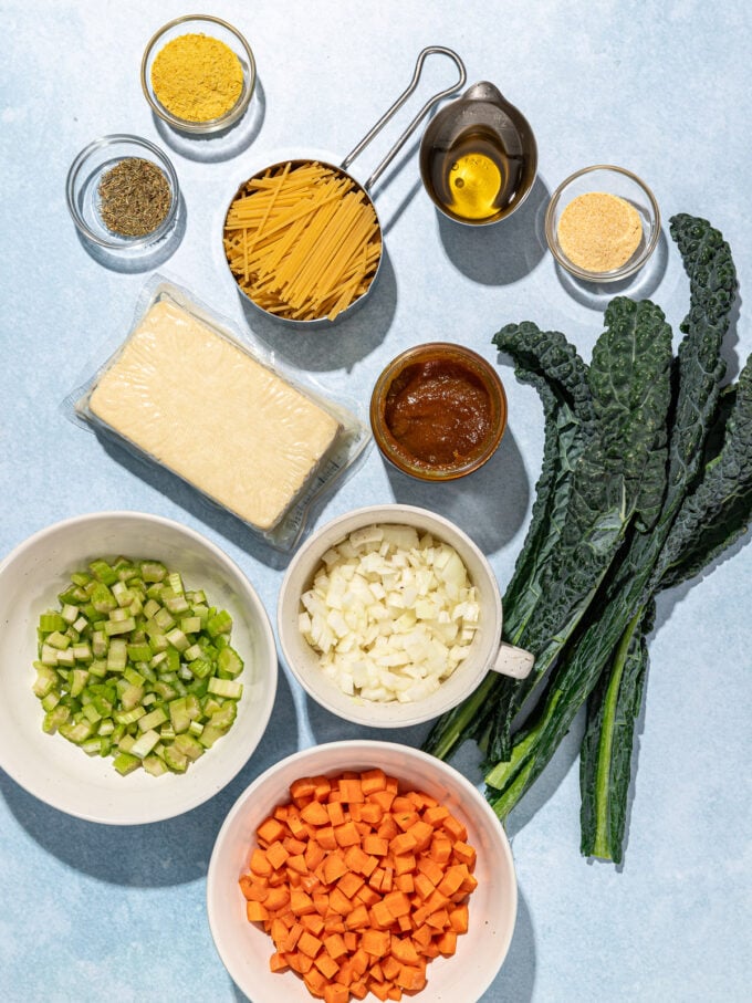 bowls of diced carrots, celery and onions with a block of tofu, broken spaghetti and seasonings