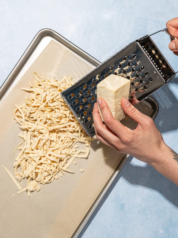 hand grating tofu onto parchment lined baking sheet