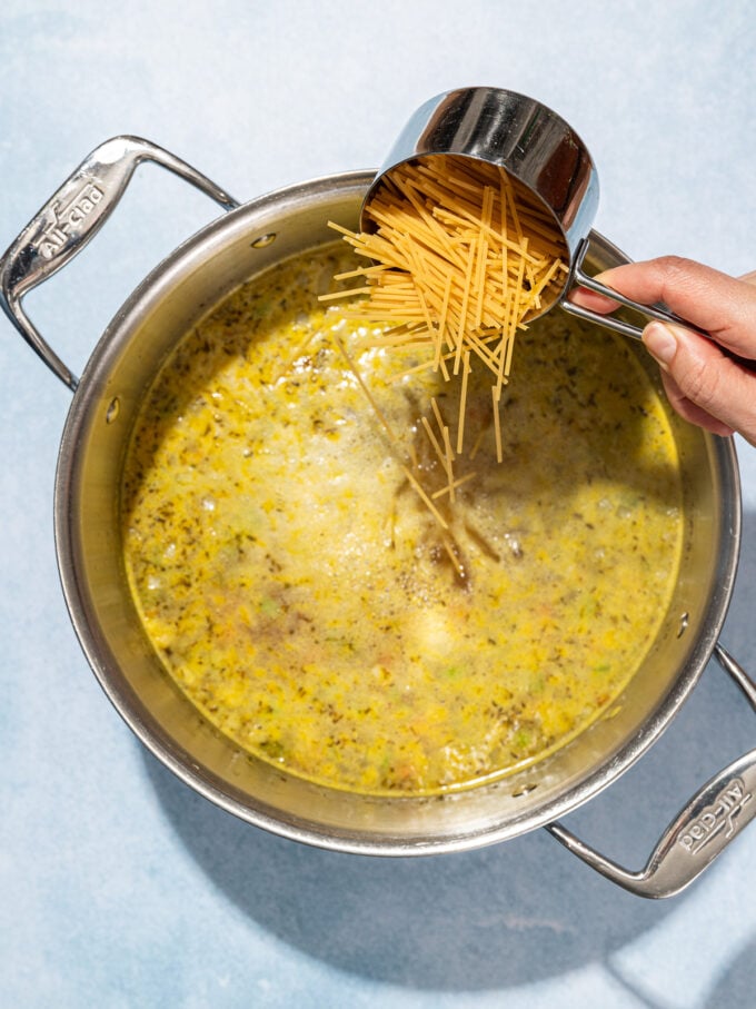 hand adding broken spaghetti to a pot of soup