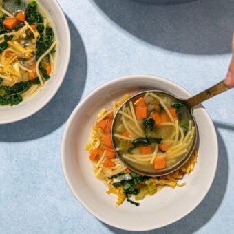 ladling vegan chicken noodle soup into white bowls