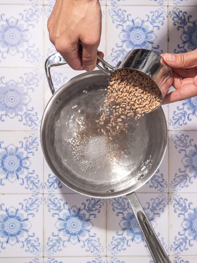 hand pouring cup of farro into pot of boiling water