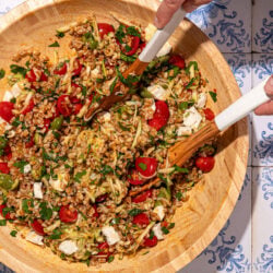 hands tossing a farro vegetable salad in a wooden bowl