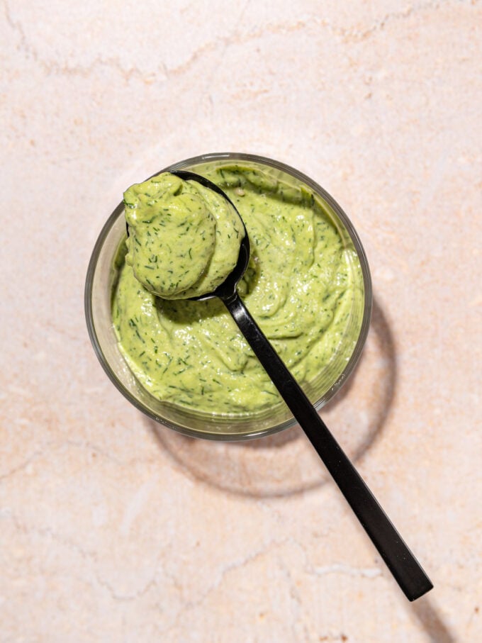 Green goddess dressing in glass bowl with black spoon resting on top
