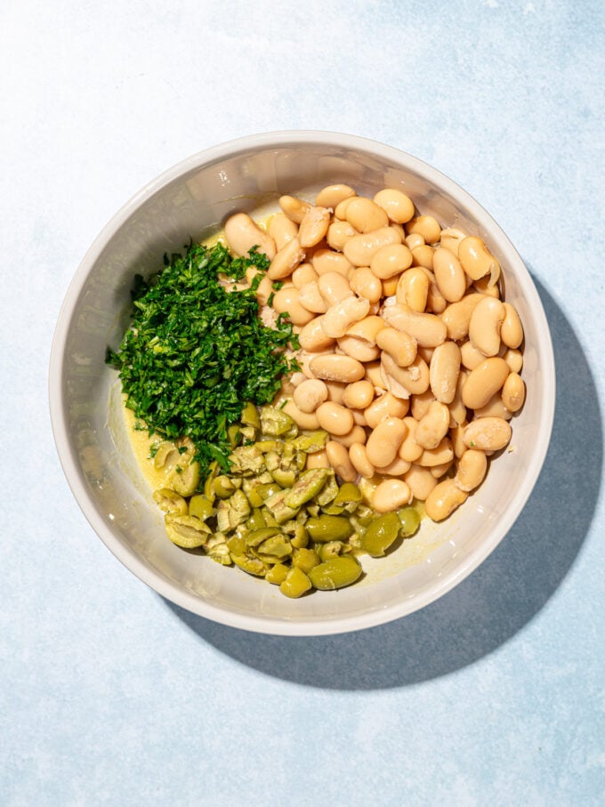 Salade de haricots blancs marinés aux olives 7 Un bol blanc avec du persil haché, du beurre et des olives à l'intérieur