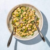 white bowl filled with marinated white bean, onion and olive salad, with two salad servers resting on top