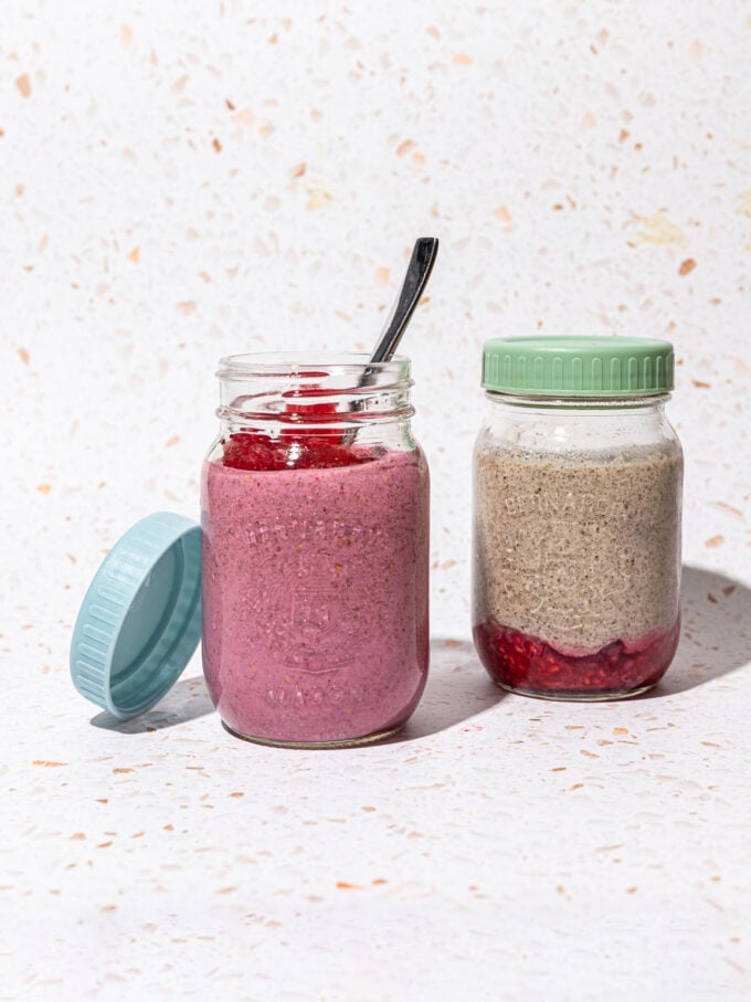 jar of raspberry blended chia pudding, with spoon resting inside, beside jar of blended chia pudding with crushed raspberries on the bottom