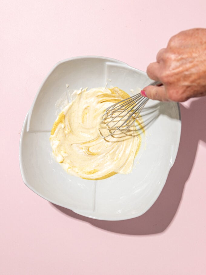 Fouetter la mayonnaise et la moutarde à la main dans un bol blanc sur fond rose