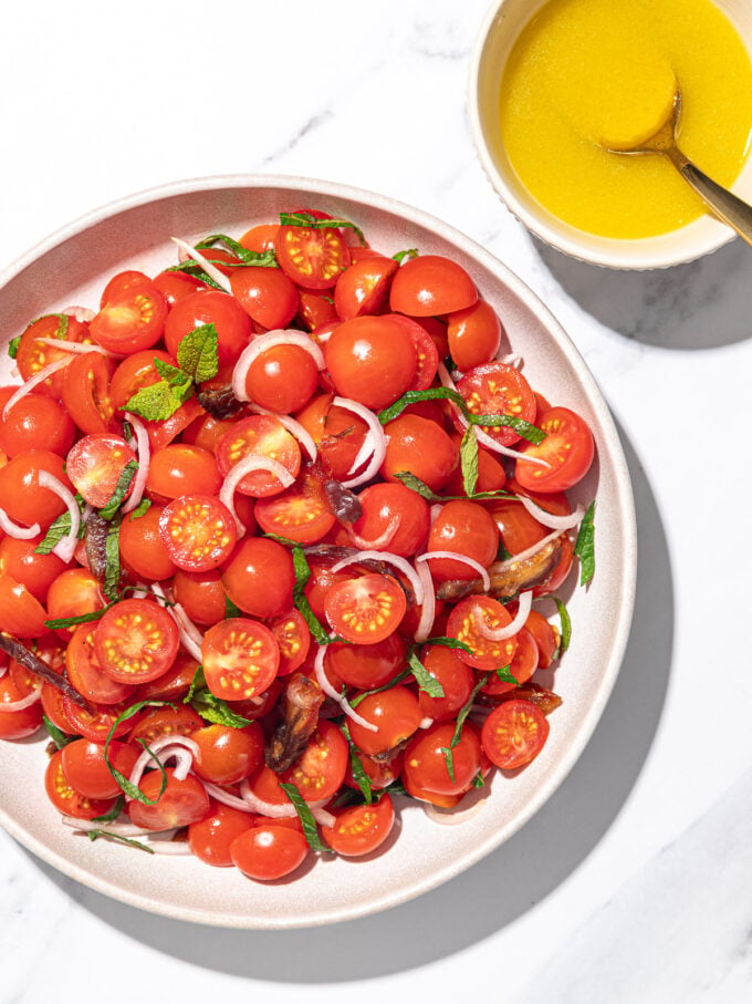 cherry tomato salad on white plate with small white bowl of garlic vinaigrette beside it