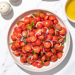 plate of cherry tomato salad with salt and pepper shakers, stacked plates and bowl of dressing beside it.