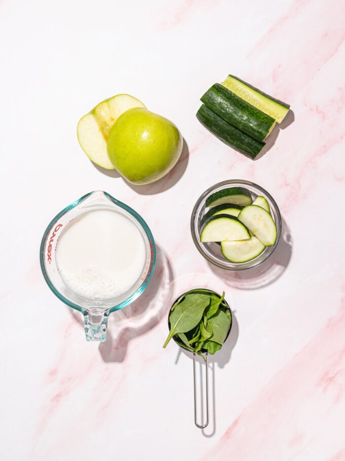 bowls of smoothie ingredients: green apple, spinach, sliced cucumber and zucchini
