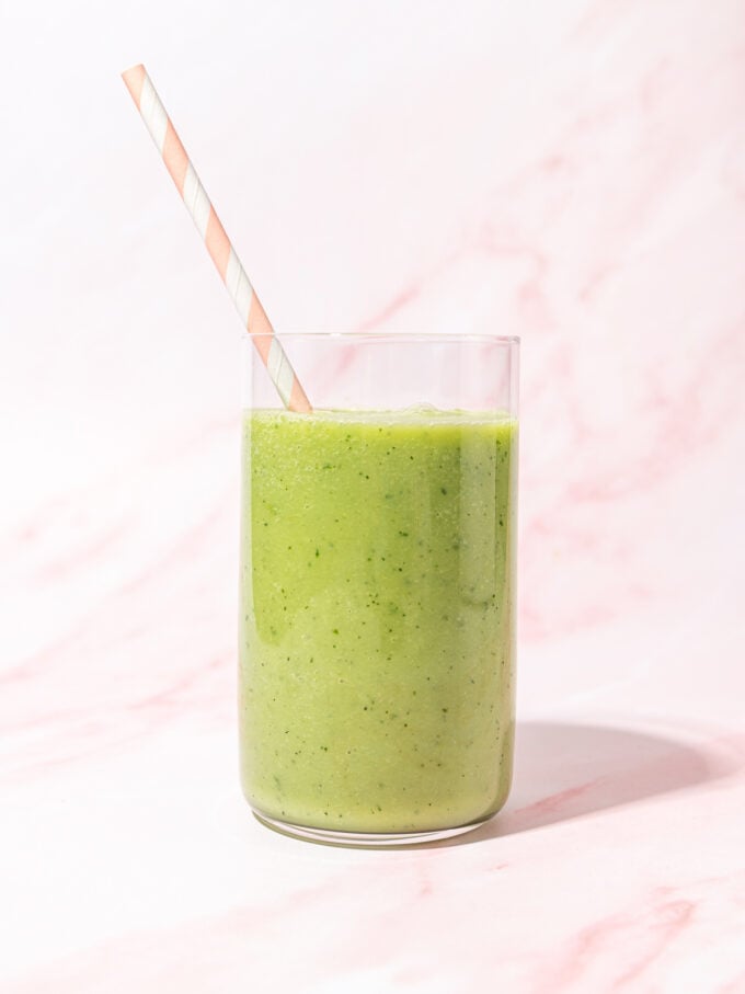 glass of green apple smoothie with pink and white straw