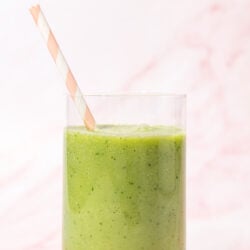 close up view of green apple smoothie in glass with pink and white straw