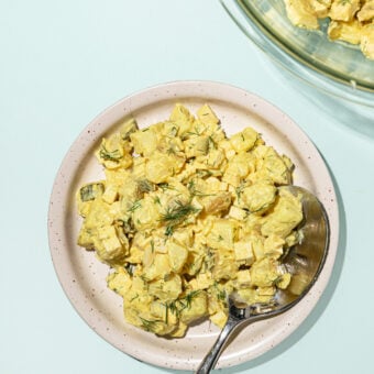 white plate topped with vegan potato salad, with a spoon.