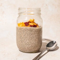 mason jar filled with chia seed pudding, topped with diced peach, with a spoon lying beside the jar
