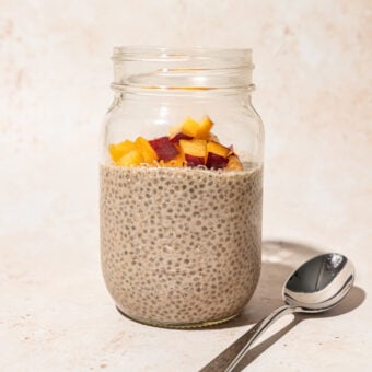 mason jar filled with chia seed pudding, topped with diced peach, with a spoon lying beside the jar