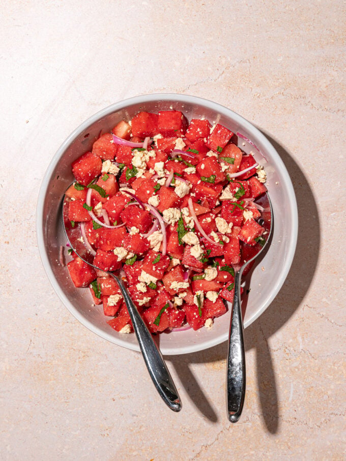 white bowl filled with watermelon mint salad with salad servers