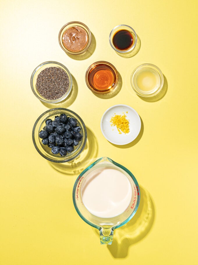 bowls of ingredients on a yellow background: soy milk, blueberries, maple syrup, chia seeds, almond butter