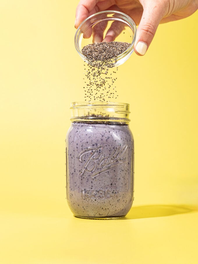 hand pouring chia seeds into mason jar with blueberry milk