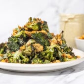 roasted broccoli with crumbled chickpeas piled high on a white plate with a glass jar of dressing and white bowl of chickpeas in the background