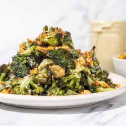 roasted broccoli with crumbled chickpeas piled high on a white plate with a glass jar of dressing and white bowl of chickpeas in the background