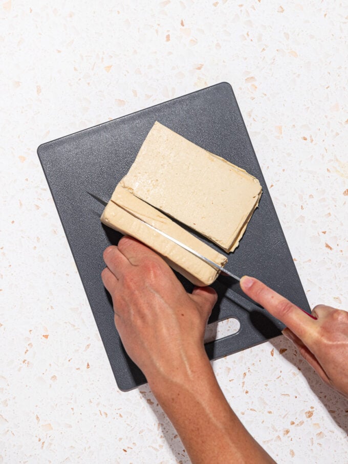 hand slicing tofu on black cutting board