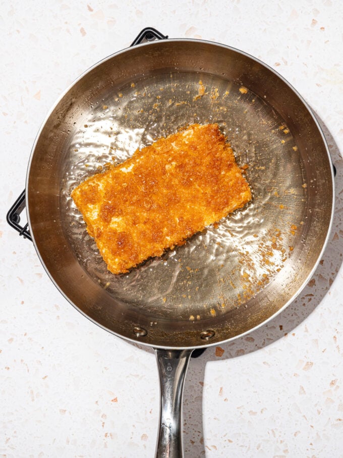 cornflake breaded tofu cutlet frying in a steel skillet