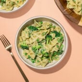 white bowls of broccoli bowtie pasta salad with wooden serving bowl and fork