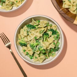 white bowls of broccoli bowtie pasta salad with wooden serving bowl and fork