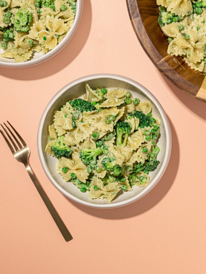 white bowls of broccoli bowtie pasta salad with wooden serving bowl and fork